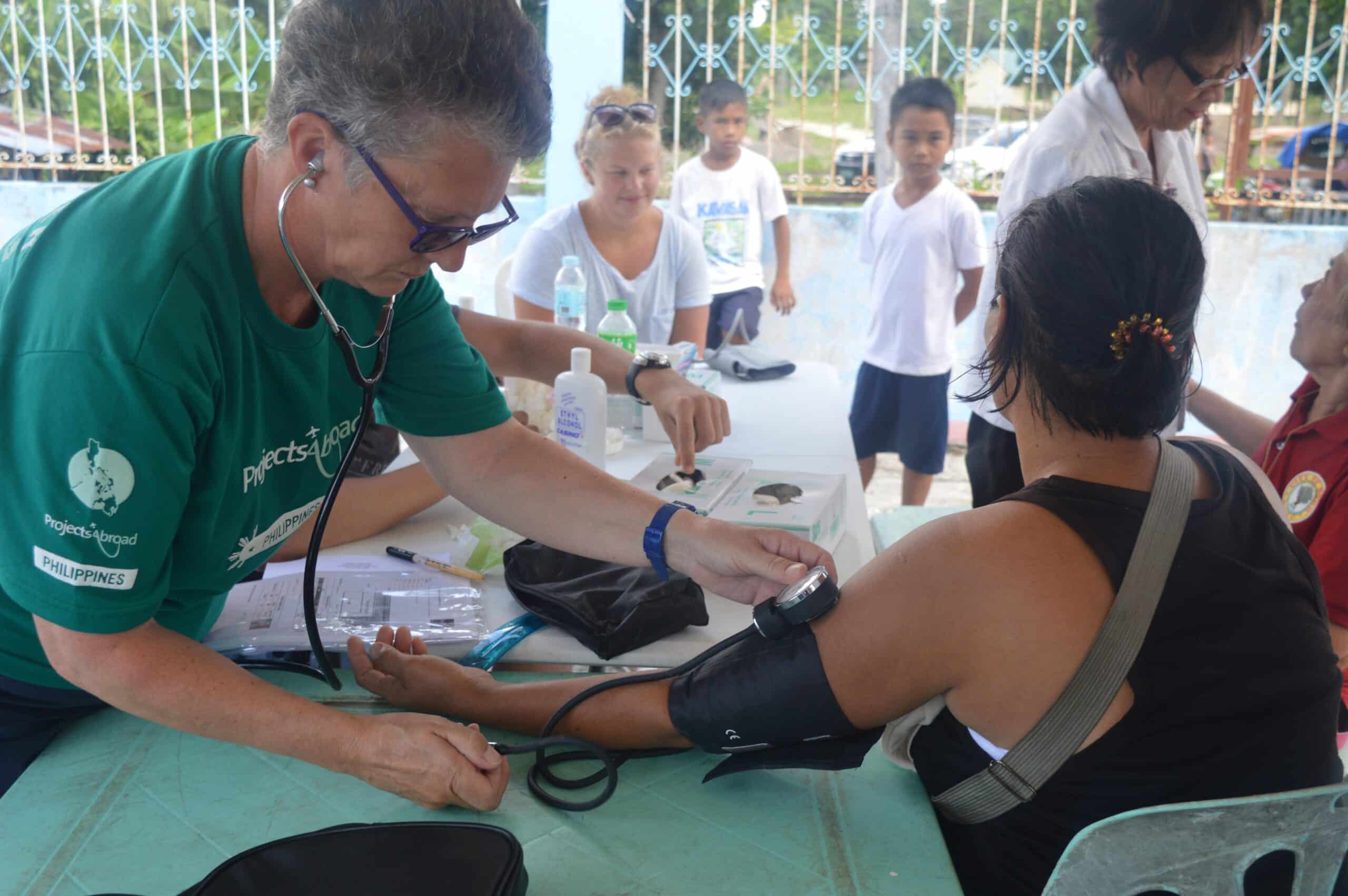 A woman participating in a volunteer abroad program for older adults in the Philippines helps a young woman at an outreach.