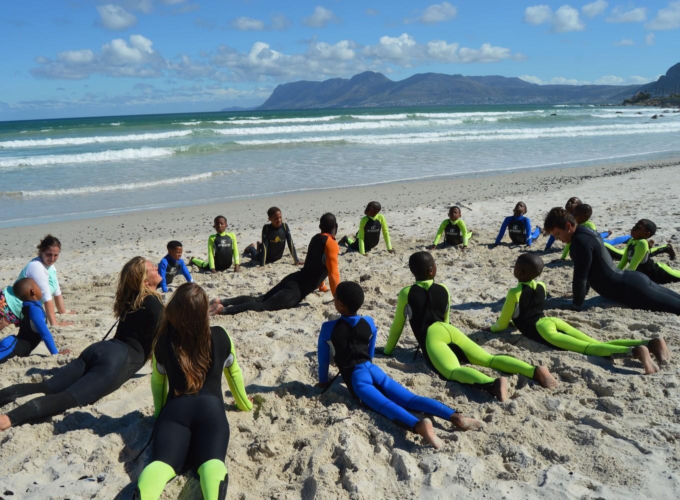 Projects Abroad volunteers stretching on the beach with children and gaining new skills at a Surfing Project