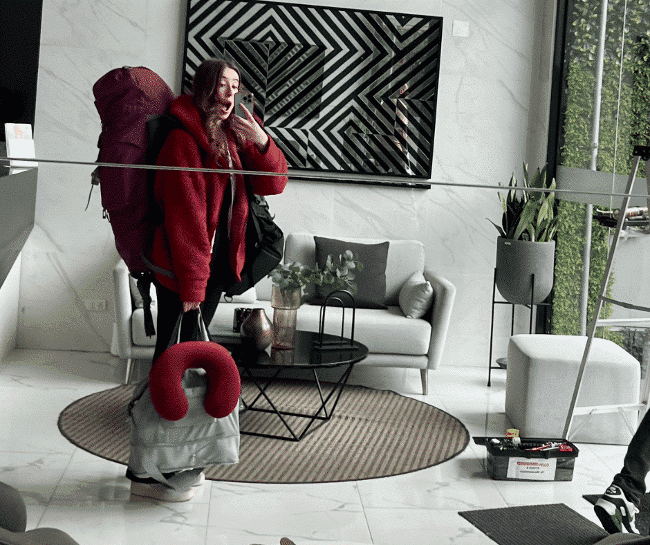 Woman taking a mirror selfie, wearing a large backpack and carrying multiple travel bags