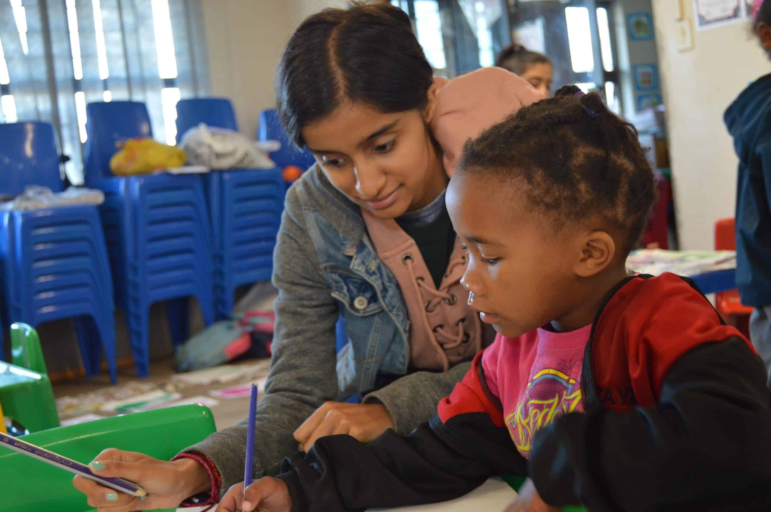 A teenager helps a child with a literacy exercise on one of our best high school volunteer abroad programmes.