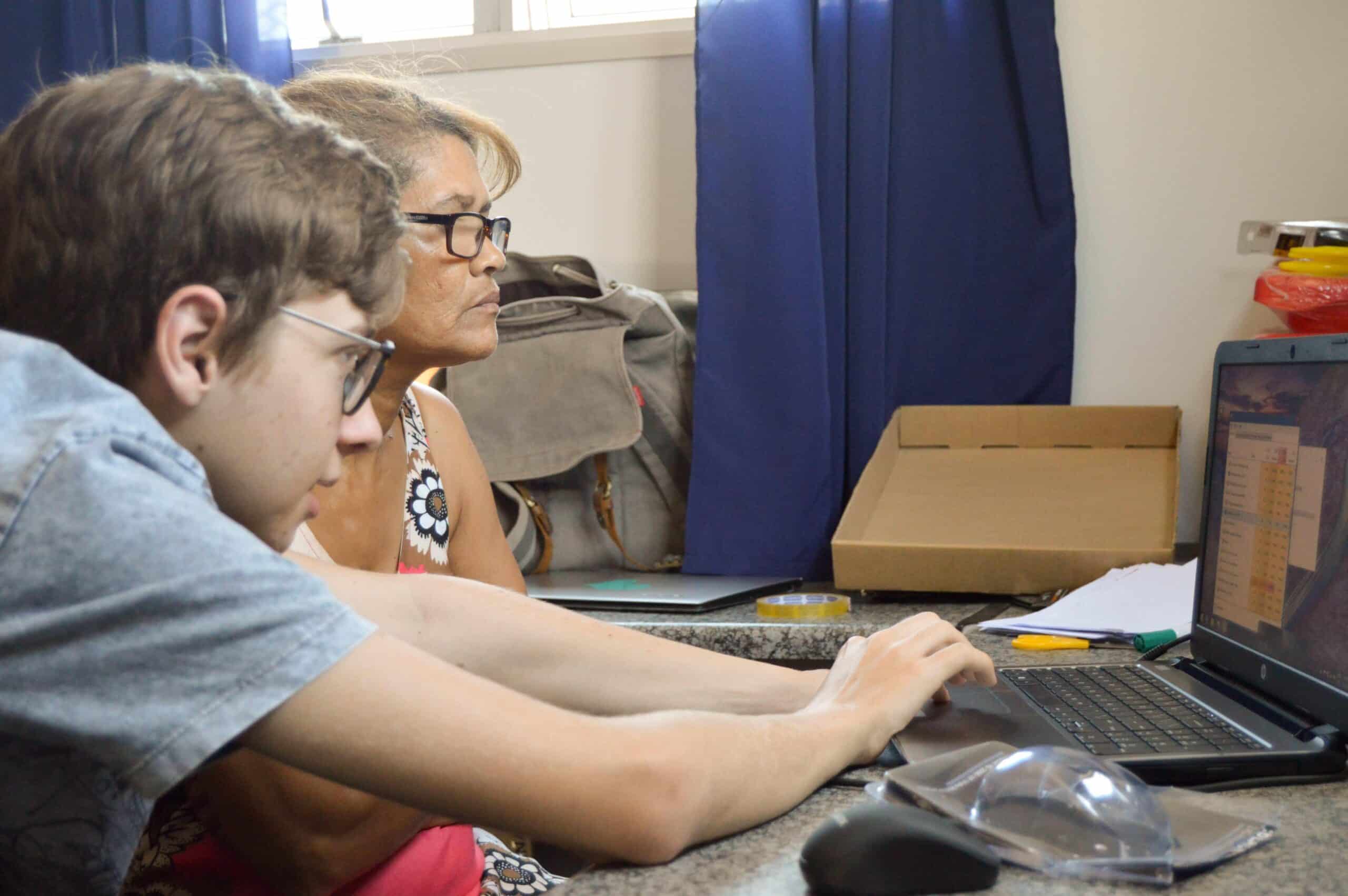 A young Projects Abroad volunteer teaches an adult woman how to use a computer program during his IT teaching internship in Ghana.